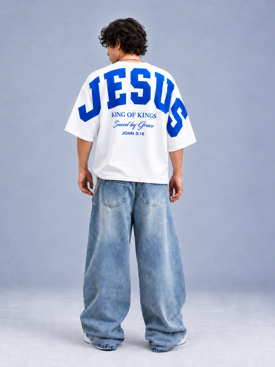 White oversized tee with varsity 'JESUS' in blue and 'King of kings, Saved by grace, John 3:16' on the back, worn with light wide-leg jeans